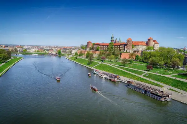 Widok na Wawel i Wisłę, najdłuższą rzekę w Polsce, z łodziami pływającymi po wodzie.