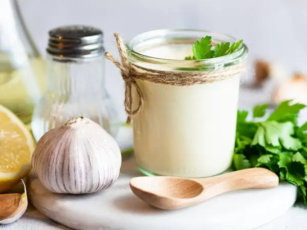 Słoik domowego aioli, czosnek, cytryna i natka pietruszki – składniki idealnego sosu.