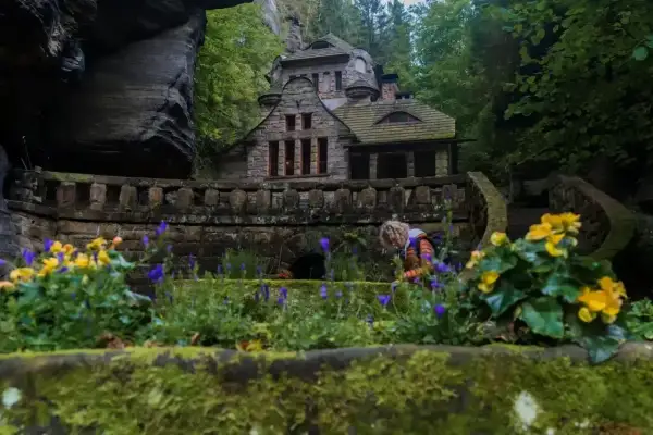 Kamienny domek w skalnym otoczeniu, idealne miejsce na czeska szwajcaria noclegi. Kwitnące kwiaty dodają uroku.