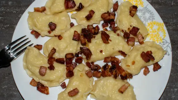 Pyszne pierogi galicyjskie posypane skwarkami z boczku, gotowe do zjedzenia. Obok leży widelec.