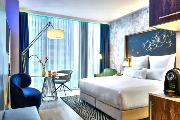 Nowoczesny pokój w hotelu NYX Warszawa: łóżko z białym pościelą, stolik kawowy, granatowe fotele i zielona sofa.