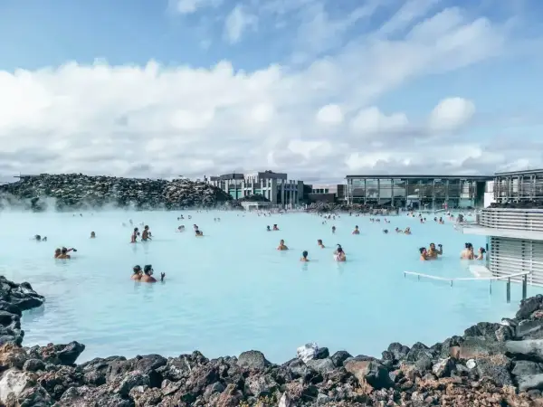 Ludzie kąpią się w turkusowej wodzie Blue Lagoon, otoczonej wulkanicznymi skałami i nowoczesnymi budynkami.