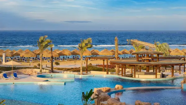 Relaks przy basenie i plaży z parasolami w hotelu Lazuli Marsa Alam. Błękitne morze i palmy tworzą rajski widok.