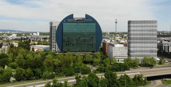 Charakterystyczny budynek Radisson Blu we Frankfurcie, otoczony zielenią, obok nowoczesnych wieżowców.