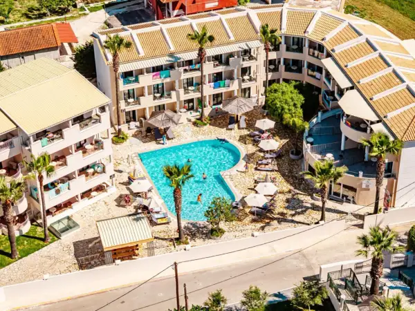 Widok z lotu ptaka na basen i budynki hotelowe. Wiele osób odpoczywa przy basenie. Warto sprawdzić caretta island hotel opinie przed rezerwacją.