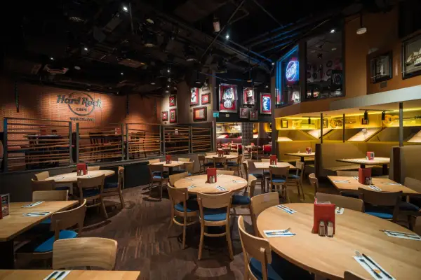Wnętrze Hard Rock Cafe Warszawa. Drewniane stoły i krzesła, ściany ozdobione pamiątkami muzycznymi i neonem "Rock Radio".