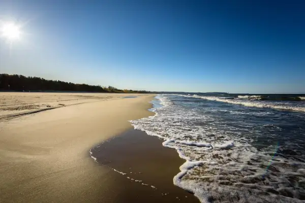 Słoneczny dzień nad polskim morzem. Piaszczysta plaża, szum fal i błękitne niebo tworzą idealny krajobraz.