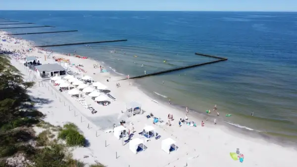 Słoneczny weekend majowy nad morzem. Ludzie odpoczywają na plaży, kąpią się w morzu i opalają pod białymi parasolami.