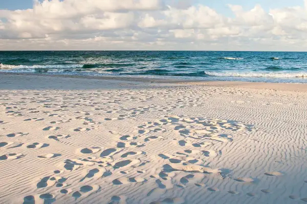 Piasek, fale i ślady stóp na plaży. Idealne miejsce, gdzie jechać nad morze na relaks.