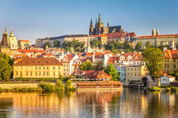 Widok na rzekę w Pradze z zamkiem na wzgórzu i kolorowymi kamienicami.
