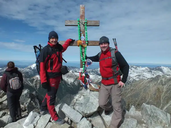 Dwóch turystów na szczycie w Tatrach Wysokich 2494 m, przy drewnianym krzyżu ozdobionym zielonymi paciorkami.