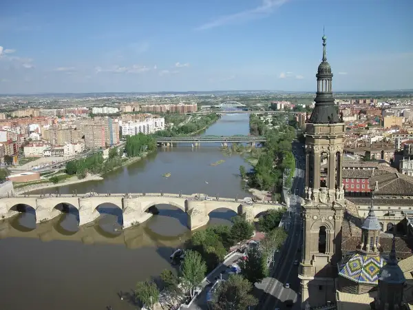 Widok na rzekę Ebro w Saragossie, z kamiennym mostem i wieżą bazyliki w tle.