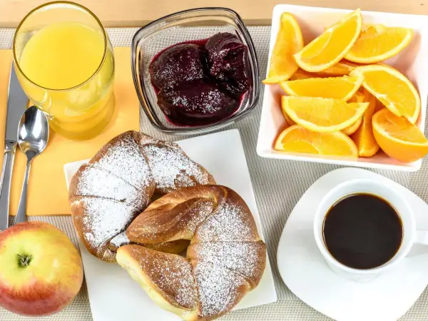 Pyszne śniadanie kontynentalne: rogaliki z cukrem pudrem, pomarańcze, dżem, sok i kawa.