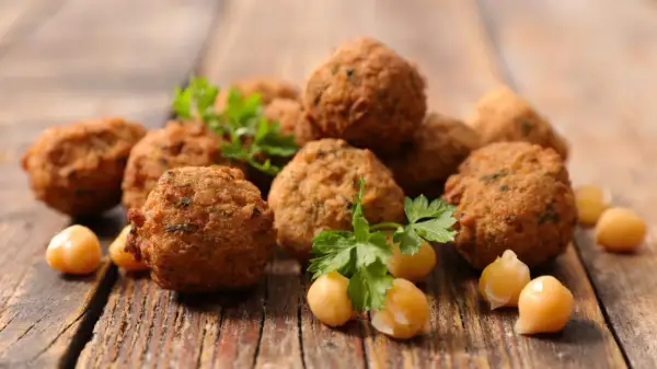 Chrupiące kulki falafel, z ciecierzycą i natką pietruszki, na drewnianym blacie. Falafel co to? To pyszna przekąska!