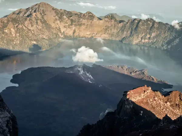Aktywny wulkan w Indonezji, z dymem unoszącym się z krateru i jeziorem w kalderze.